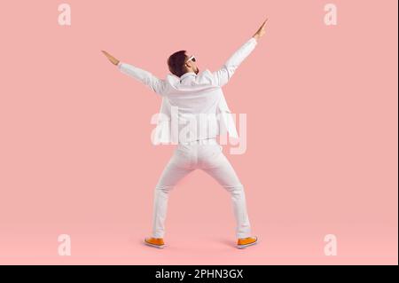 Funny inspired man in white suit performs energetic fashionable dance back to camera Stock Photo