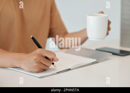 Closeup image of young man drinking cup of morning coffee and writing down plans for the day Stock Photo
