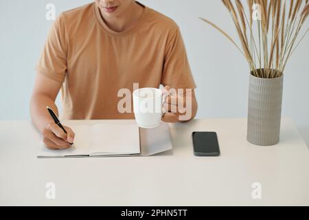 Man drinking morning coffee and writing in planner Stock Photo