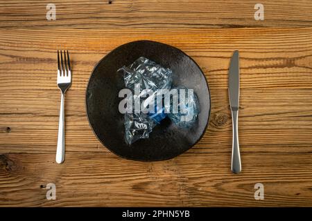 Eat Plastic, Blue Empty Plastic Bottle on Plate, Crumpled Plastic Bottle, Global Pollution Concept, Squashed Water Pet Bottles on Wood Background Stock Photo