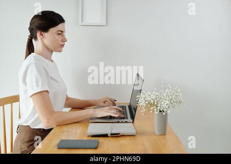 Serious young woman working on laptop at desk in her home office Stock Photo