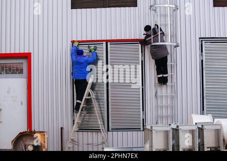 Workers installing window shutters with blinds on house or industrial building. Stock Photo