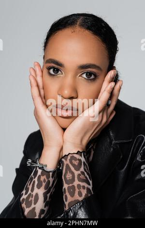 portrait of charming african american woman in trendy clothes touching face and looking at camera isolated on grey,stock image Stock Photo