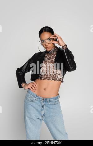 slender african american woman in cropped jacket and trendy sunglasses posing isolated on grey,stock image Stock Photo