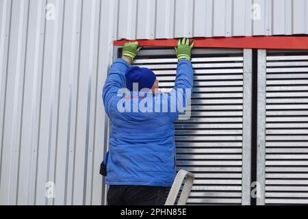 Worker installing window shutters with blinds on house or industrial building. Stock Photo