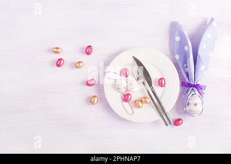 Easter table setting. White plate with a napkin folded in the shape of a rabbit, Easter and chocolate eggs on a pink background. Happy Easter holiday Stock Photo