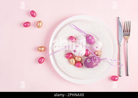Happy Easter. Table setting for Easter holiday. Easter eggs, flower and cutlery on pink background. Top view, flat lay Stock Photo