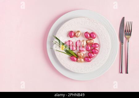 Happy Easter. Table setting for Easter holiday. Easter eggs, flower and cutlery on pink background. Top view, flat lay Stock Photo