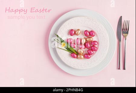 Happy Easter. Table setting for Easter holiday. Easter eggs, flower and cutlery on pink background. Top view, flat lay Stock Photo