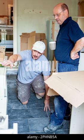 Kitchen Fitters: Working Together. A pair of workers pulling together to resolve an issue on their new kitchen build. From a series of related images. Stock Photo