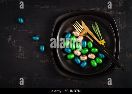 Happy Easter. Table setting for Easter holiday. Easter chocolate eggs and cutlery on dark background. Top view, flat lay Stock Photo