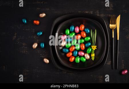 Happy Easter. Table setting for Easter holiday. Easter chocolate eggs and cutlery on dark background. Top view, flat lay Stock Photo