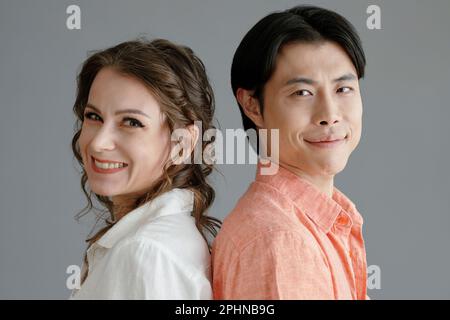 Happy middle-aged woman and young man standing back to back and smiling at camera Stock Photo