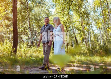 Senior family couple walking outdoors in summer forest. Elderly people holding hands. Romantic date. Man and woman enjoy landscape Stock Photo