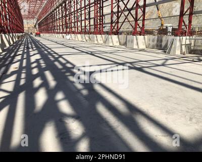 Truss ceiling and metal pillars and girders cast shadow on concrete floor. Support constructions. Industrial building metal framework. Low angle view Stock Photo