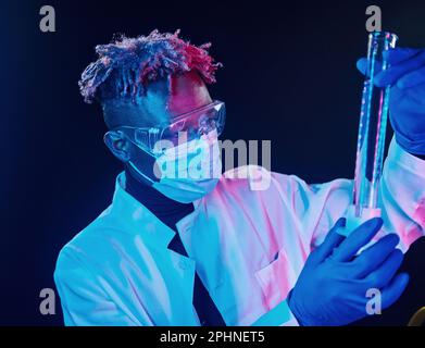 Smart scientist in protective uniform holding test tube. Coronavirus conception. Futuristic neon lighting. Young african american man in the studio Stock Photo