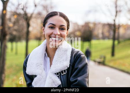 Caucasian beauty beaming in casual attire, posing at park with cityscape sunset view, radiating charm with a captivating smile. Stock Photo
