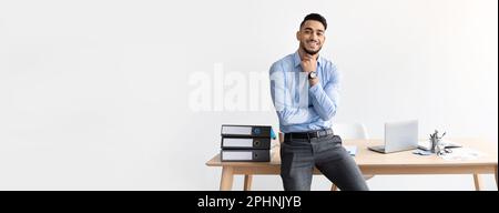 Smiling handsome successful confident arabic young businessman think sit table in office Stock Photo