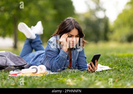 Worried Young Arab Female Reading Message On Smartphone While Relaxing Outdoors Stock Photo