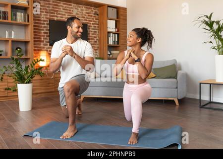 Smiling handsome young black lady and guy in sportswear doing leg exercises on workout, enjoy fit Stock Photo