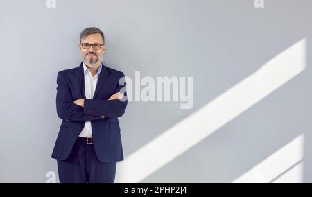 Happy handsome businessman in a dark blue suit stands with his arms crossed on his chest. Stock Photo