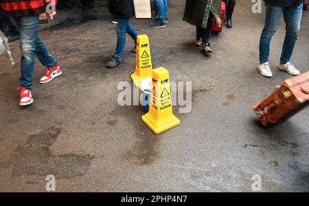 London, United Kingdom - February 01, 2019: Yellow cone with caution wet floor sign, on asphalt road, people walking around, detail to their feet only Stock Photo