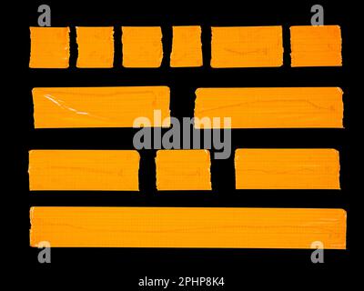 A collection of various torn pieces of orange adhesive tape isolated on a black background Stock Photo