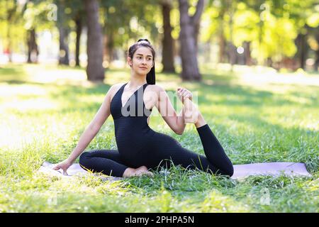 Young pregnant woman leading an active lifestyle and practicing yoga, performs a variation of the exercise Eka Pada Rajakapotasana, dove pose, trains Stock Photo