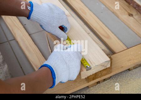 A man in white construction gloves measures a pine board with a tape measure Stock Photo