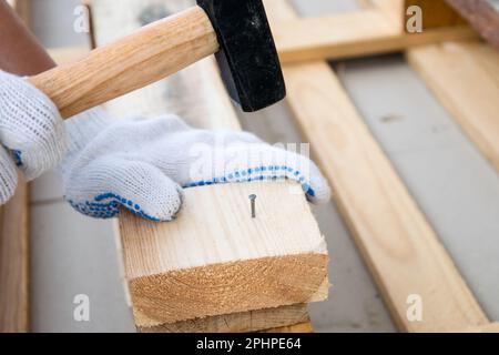 A man in white construction gloves is hammering a nail into a wooden board Stock Photo