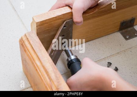 A little boy unscrews the wooden table with a screwdriver Stock Photo