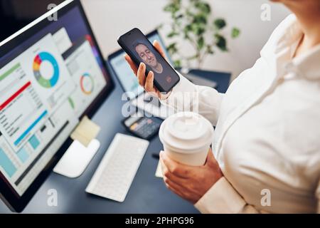 Businesswoman having video chat on mobile phone with her colleague. Businesswoman working with data on charts, graphs and diagrams on computer screen. Stock Photo