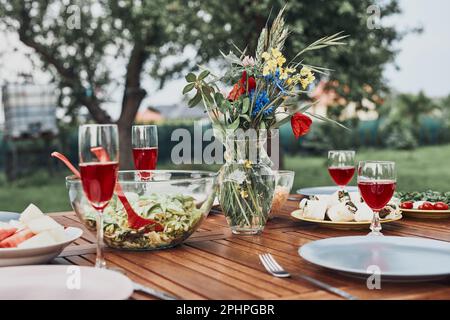 Dinner in an apple orchard garden on wooden table with salads and wine decorated with flowers. Close up of table with food prepared for family dinner Stock Photo