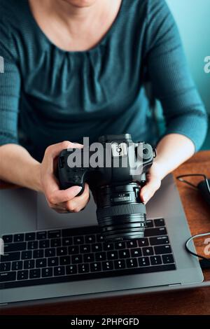 Female photographer working on photos on laptop and camera. Woman editing retouching browsing photos working as a freelancer sitting at desk Stock Photo