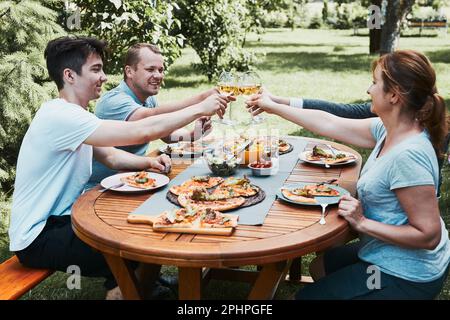 Friends making toast during summer picnic outdoor dinner in a home garden. Close up of people holding wine glasses with white wine over table with piz Stock Photo