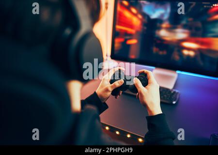 Man playing video game at home. Gamer holding gamepads sitting at front of screen. Streamer playing online in dark room lit by neon lights. Competitio Stock Photo