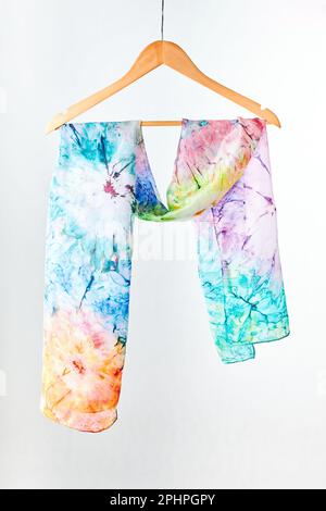 Silk colourful hand painted tied scarf hung on hanger over grey background. Woman fashion, tying a scarf, wearing a scarves. Stylish ways to tie and w Stock Photo