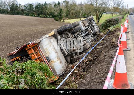 Killough, Northern Ireland: 12/02/2023.  Bin lorry lies overturned in a field after leaving the road and rolling down a slope. Stock Photo