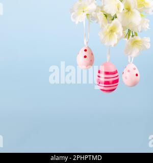 Three beautiful pink Easter eggs hanging from a flowering branch on a serene blue backdrop, a perfect image of hope and renewal Stock Photo