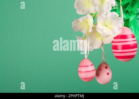 Picturesque scene of Easter festivities, featuring three pink easter eggs dangling from a decorated branch against a beautiful green backdrop Stock Photo