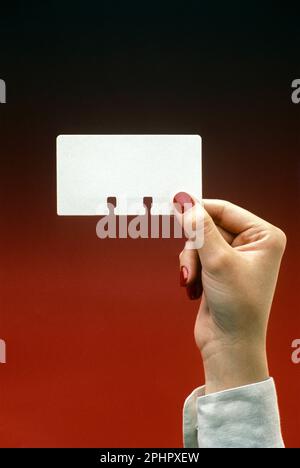 1991 HISTORICAL WOMAN’S HAND HOLDING UP ROLODEX CARD (©ARNOLD NEUSTADTER 1956) ON PLAIN RED BACKGROUND Stock Photo