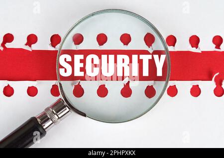 Between two sheets from a notebook on a red stripe with the inscription - security, there is a magnifying glass. Stock Photo