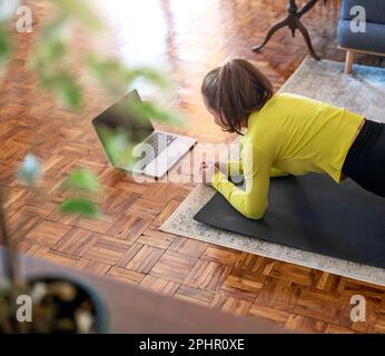 Online sport training at home, woman doing plank and using her laptop. Stock Photo