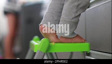 Child on tiptoes at kitchen helping mother. Infant one year old baby feet on tiptoe Stock Photo