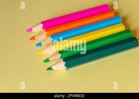 several colored pencils lined up on a pastel yellow background Stock Photo