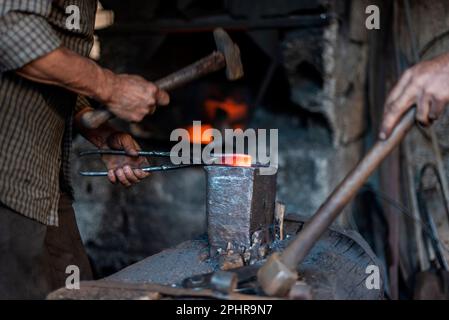 A blacksmith is making iron tools with hammer in a workshop, close up Stock Photo