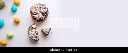 Banner of Easter Kraffin on light background with colored, bright eggs. Cake with candied fruits, raisins, chocolate, nuts, topping with powdered suga Stock Photo