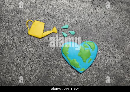 Happy Earth Day. Flat lay composition with plasticine planet and watering can on grey table Stock Photo