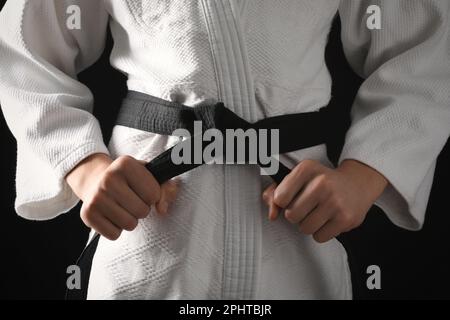 Man in keikogi with black belt on dark background, closeup. Martial arts uniform Stock Photo