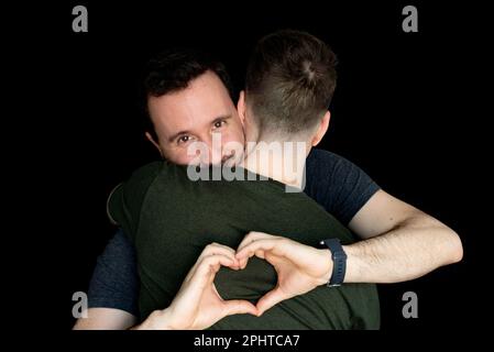 Young gay couple making a heart shape with his hands isolated on black background. Stock Photo
